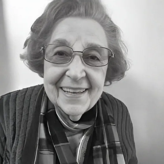 Person wearing a quilted jacket and a patterned scarf, posed in front of a plain light-colored background in a black‑and‑white portrait.