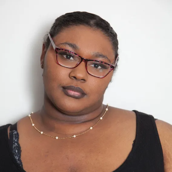 Person wearing a black tank top and a delicate gold necklace with small beads, posed against a plain white background.