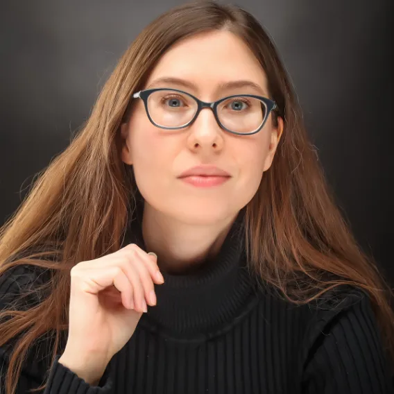 Person wearing a black ribbed turtleneck sweater, seated against a dark studio backdrop with long hair draped over the shoulders