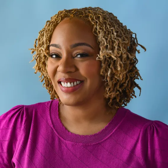 Person wearing a bright magenta sweater, shown against a solid light blue background with shoulder‑length textured hair.