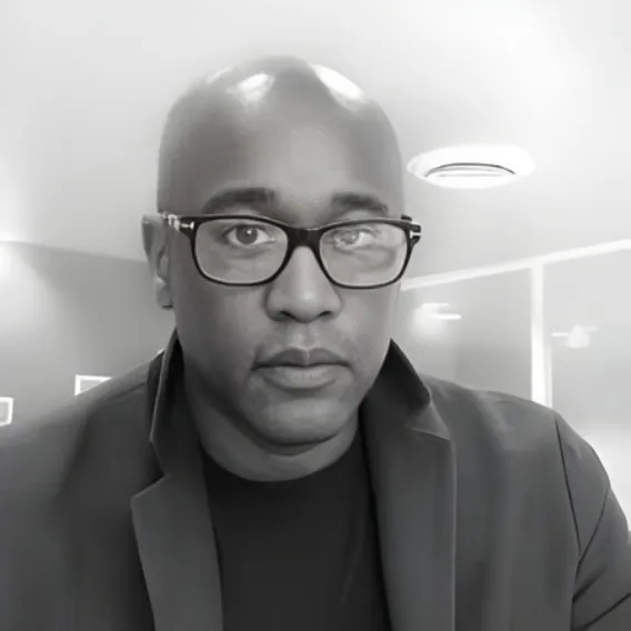 Person wearing a dark jacket and shirt, seated indoors in a bright room with modern ceiling lights and glass partitions