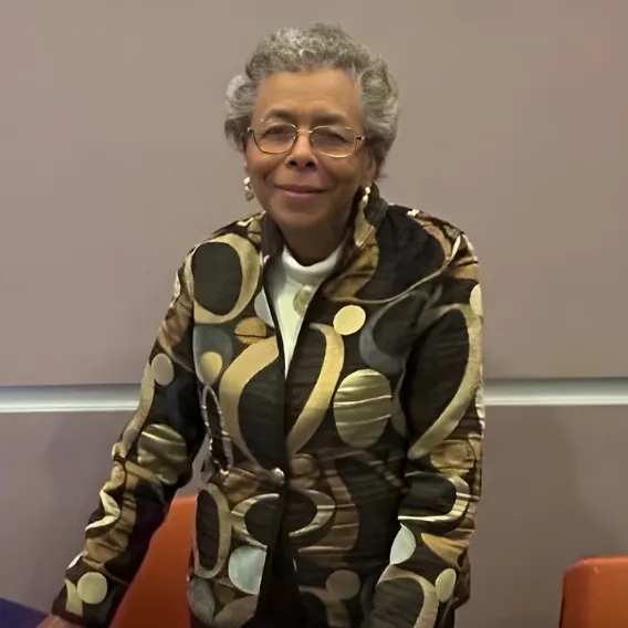 Person wearing a patterned jacket with circular and curved designs, standing near a table in an indoor setting