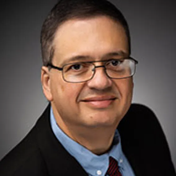 male with glasses, black jacket blue shirt and red tie 