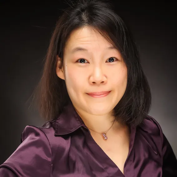 Professional headshot of woman with medium-length black hair, wearing a purple blouse. 