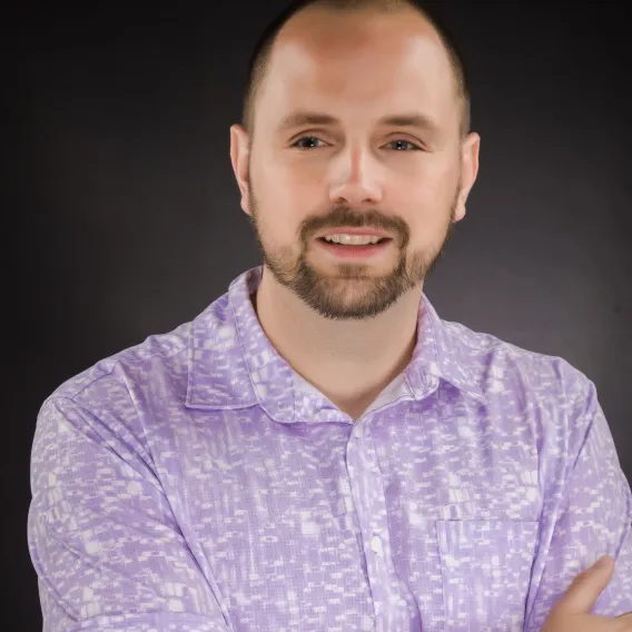 Professional headshot of man with short beard, wearing a purple and white shirt