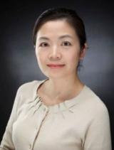 Headshot of an Asian woman in a light cardigan with a dark background.